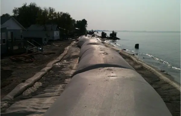 Large geotextile breakwater tubes installed along a coastline to prevent wave-induced erosion and stabilize the shoreline